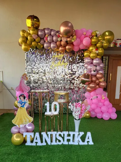 A princess theme party with a silver shimmer wall backdrop. The setup includes a pink and gold balloon arch and cutouts for a glamorous photo area.