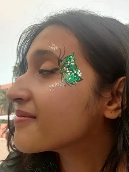 A vibrant green butterfly with white polka dots and a sprinkle of glitter. It's a playful and eye-catching piece of face art.