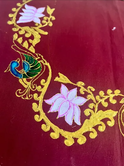 A close up of a beautiful peacock and lotus border painted on fabric in the Tanjore style, perfect for decorating textiles.