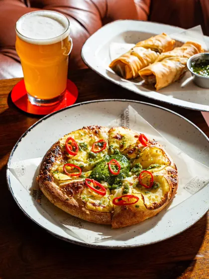 The potato pizza paired with a glass of beer and other appetizers, creating a full pub-style scene.