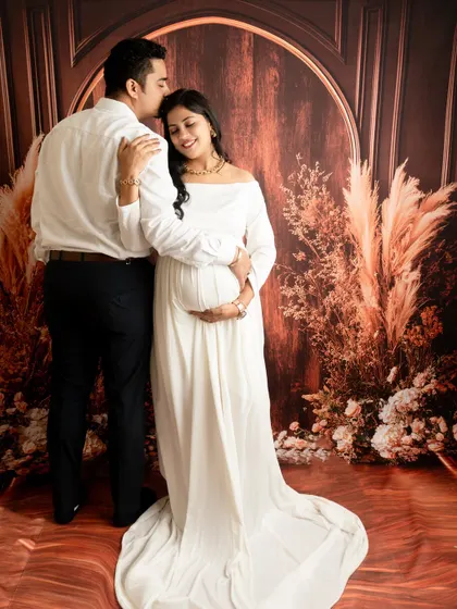 A tender moment captured. The husband's gentle kiss on the forehead adds a layer of warmth and emotion to the maternity portrait.