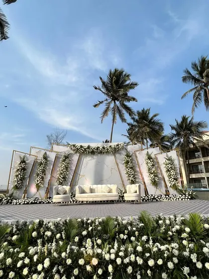A modern, geometric stage setup for a Christian beach wedding, with all-white florals and palm trees in the background.