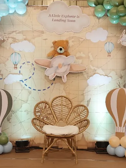 The central photo spot for the travel-themed shower, featuring a cute teddy bear pilot and a rattan peacock chair for the mom-to-be.