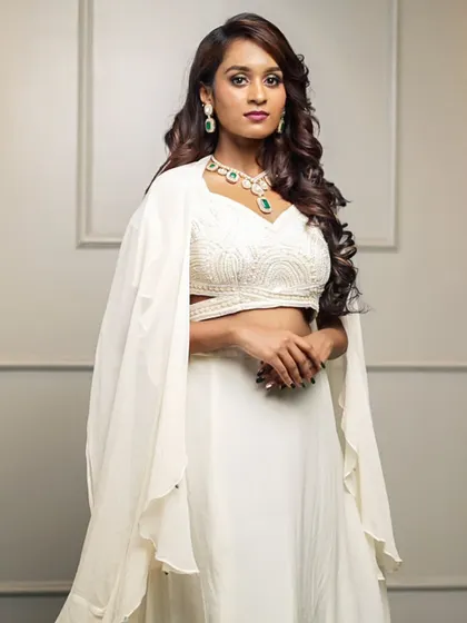 For a modern and chic statement, we offer this white fusion lehenga set. The intricately embroidered crop top is paired with a simple skirt and a dramatic, flowing cape for a truly contemporary ethnic look.