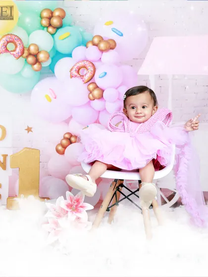 Dressed in pink, this little girl is the star of her donut-themed first birthday shoot. The vibrant balloon arrangement adds a festive touch to her milestone portrait.