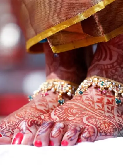 A close-up of the bride's feet, adorned with beautiful anklets and intricate Mehndi. We believe in capturing every detail of the bridal attire.