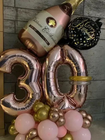 A compact and stylish balloon arrangement for a 30th birthday. It features rose gold "30" foil numbers, a champagne bottle foil balloon, and a base of pink and chrome balloons.
