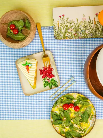A cheerful tablescape with a blue gingham cloth and a variety of colorful plates and bowls. This flatlay is perfect for a spring or summer collection.