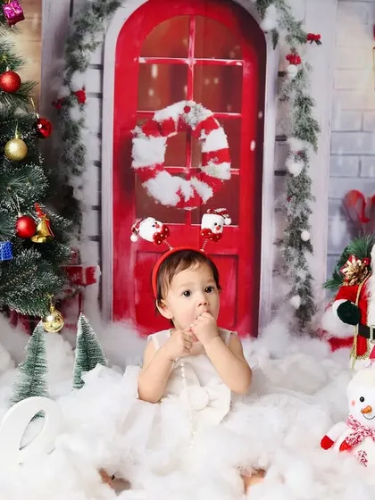 A wider view of the Christmas first birthday setup, showing the little girl surrounded by a tree, snowman, and candy canes.