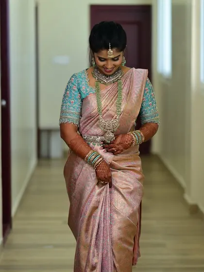 A full-length shot of the bride walking down a corridor, showcasing the elegant combination of her saree and custom blouse.