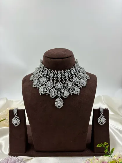 A heavy, silver-plated AD necklace set with a peacock-inspired feather design. This statement piece is available in blue, green, pink, and all-white.