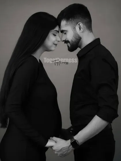 A classic black and white portrait of the couple. They stand forehead-to-forehead, holding hands over the baby bump, a timeless image of togetherness.