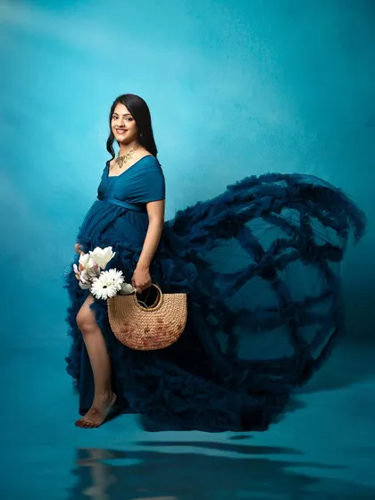 Another beautiful shot from the same maternity session. The makeup remains flawless, and the styling creates a soft, ethereal look against the blue backdrop.