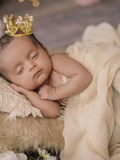 A sleeping prince. This close-up shot focuses on the baby's peaceful face, adorned with a tiny crown, in a cozy, neutral-toned bed.