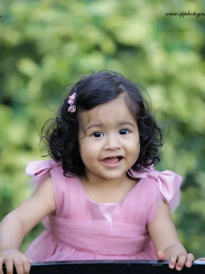 This outdoor portrait of a toddler in a lovely pink dress captures her bright smile and cheerful personality against a natural green background.