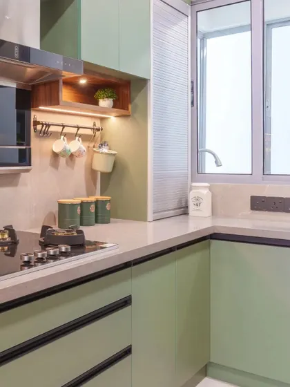 A close-up of the hob area in the sage green kitchen, showing the wooden open unit for mugs and small plants, adding a touch of warmth and life.
