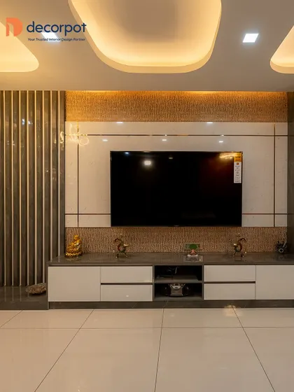 A bold and dramatic TV unit featuring a textured stone-finish backdrop and fluted side panels. The clean white console provides a stark, beautiful contrast, while the unique false ceiling adds another layer of design.