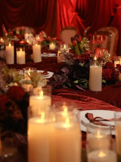 A long view of the candlelit dining table. The repetition of candles and floral centerpieces creates a sense of rhythm and abundance, making the dinner feel truly special.