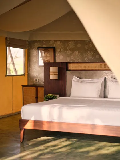A detail shot of the bedroom in a Fireflies Resort tent. The play of light and shadow, combined with natural materials like wood and cane, creates a warm and inviting atmosphere for guests.
