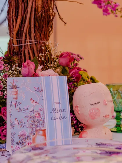 A close-up of a tabletop detail, featuring a whimsical, face-shaped vase and a custom-printed 'Mint to be' card. These artistic touches make the decor unique and memorable.