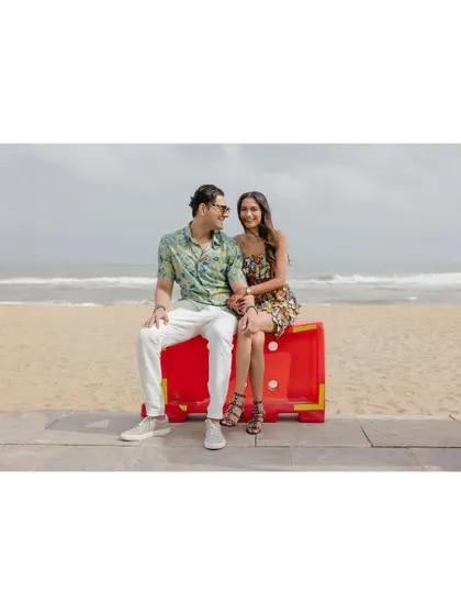 A candid portrait of Saumya and Sid on a bright red beach barricade. The vibrant color and their relaxed pose create a fun, modern, and slightly quirky wedding portrait.