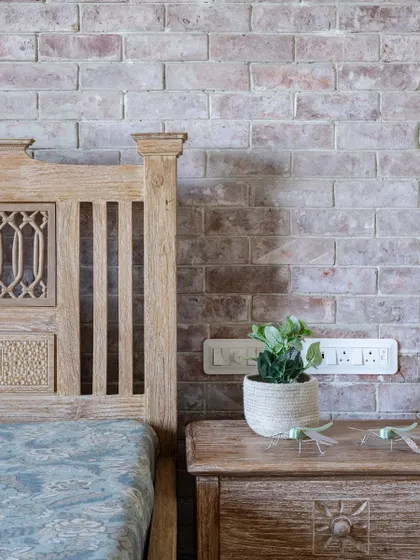 A close-up of the bedroom, showing the texture of the whitewashed brick wall against the intricately carved wooden bed frame. Small details, like the dragonfly ornaments, add a touch of whimsy.