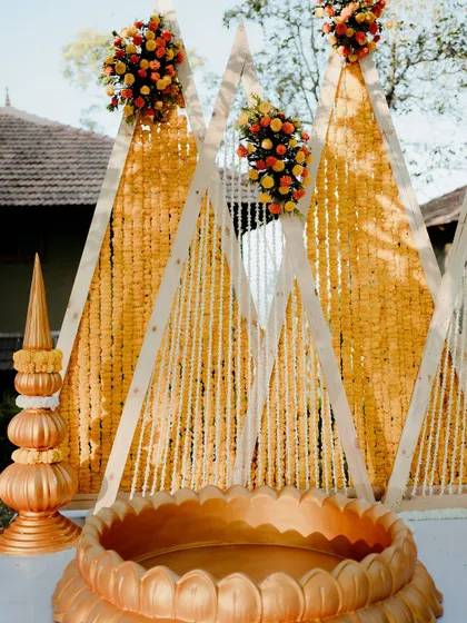 This modern Haldi setup features a unique triangle backdrop adorned with marigold and tuberose garlands. The geometric design adds a fun and contemporary twist to the traditional ceremony.