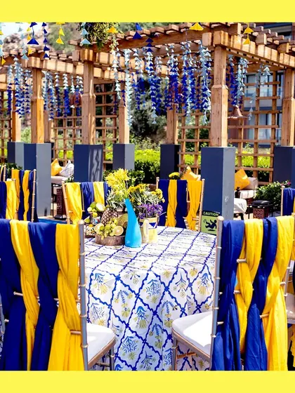 A view of the guest dining tables. The chairs are draped in alternating blue and yellow fabric, and the tables feature a traditional blue and white patterned cloth, tying the whole theme together.