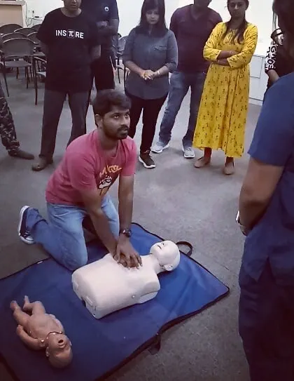 A student practices chest compressions on a CPR mannequin under the watchful eye of fellow participants.