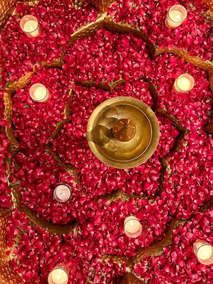 A top-down view of a brass urli filled with red rose petals and floating candles, a classic and beautiful decor element.