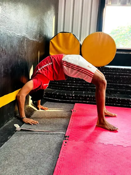 A student practices a wall-assisted backbend. This is a great drill for beginners to build the necessary strength and flexibility.