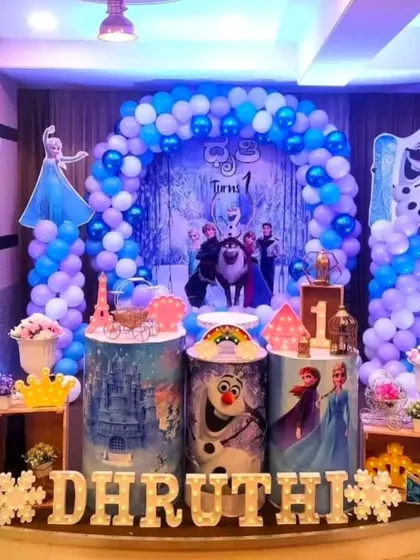 Let it go with our Frozen themed party decor. This setup for Shashtika's first birthday features Elsa, Anna, and Olaf with a blue and purple balloon arch that looks like a winter wonderland.
