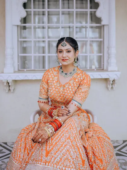 A seated portrait of the bride, showcasing her full lehenga and the intricate details of her jewelry.