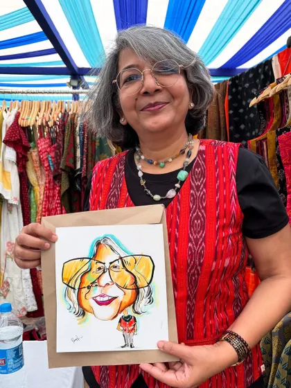 An elegant guest at the Earth Mela, holding her caricature which captures her style perfectly.