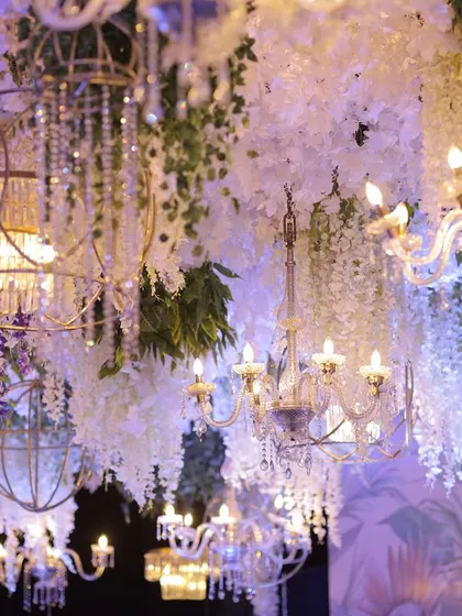 A ceiling dense with hanging white wisteria, crystal birdcages, and classic chandeliers. This intricate overhead installation creates a sense of opulence and enchantment.