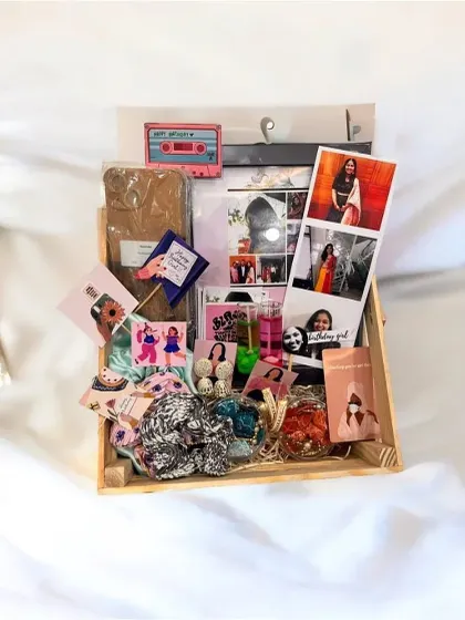 A look at a fully loaded birthday hamper, all arranged in a rustic wooden tray. This gift set includes a custom frame, jhumka earrings, candles, polaroids, scrunchies, and personalized wallet cards.