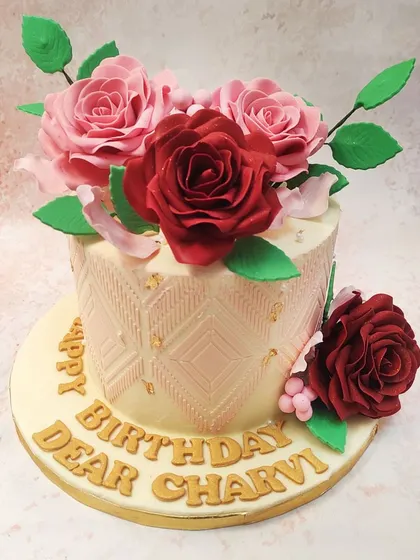 We design a birthday cake for a wife that speaks of love and appreciation. This elegant cake features an embossed geometric pattern and is crowned with a stunning bouquet of handcrafted red and pink edible roses, making it a truly special gift.