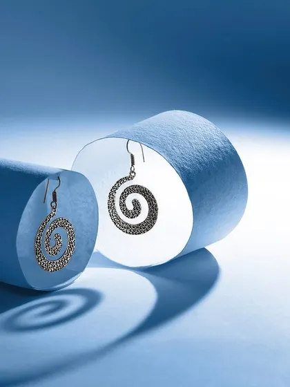 A conceptual photograph of two spiral earrings, using rolled paper and dramatic lighting to create interesting shadows and depth. This abstract approach is great for editorial or brand-building imagery.