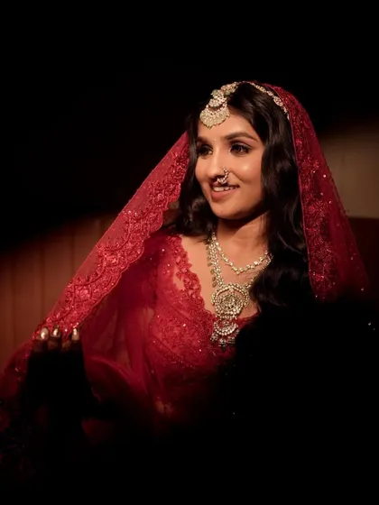 A dramatic and beautiful shot of the bride under her red veil. The lighting highlights her glowing skin and defined eyes, creating a timeless and artistic bridal portrait.