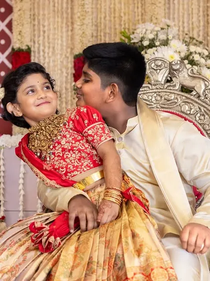 A sweet, candid moment between two children in traditional outfits during a ceremony, capturing their innocent interaction.