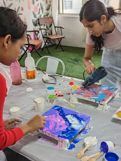 Two participants working on their pour paintings, using a hairdryer to create unique fluid patterns.
