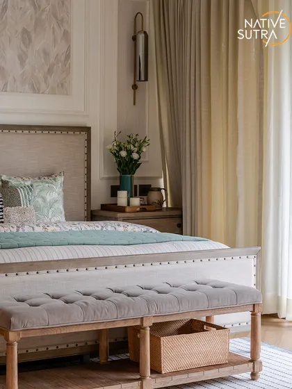 A close-up of the bed and tufted bench, showcasing the blend of classic and rustic elements. The studded, linen-upholstered bed frame and wall mouldings add a touch of sophistication to this inviting sanctuary.