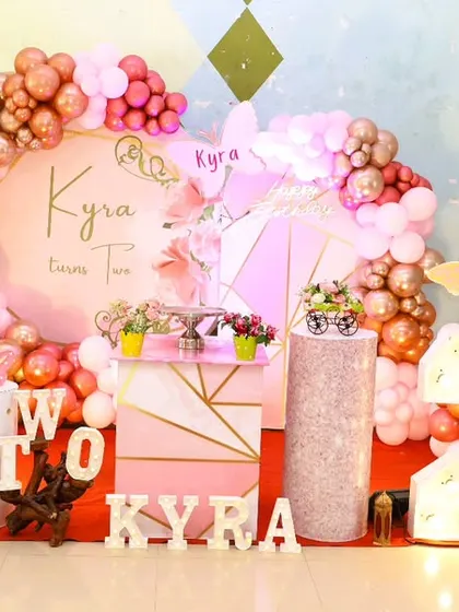 A full stage setup for a butterfly-themed 2nd birthday, with a custom backdrop, marquee 'TWO', and a pink and rose gold color scheme.