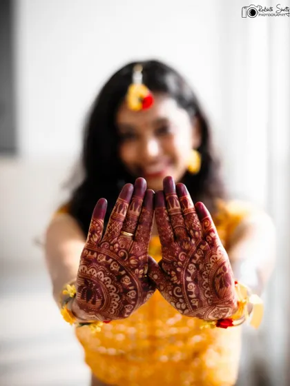 A creative Haldi shot focusing on the bride's intricate mehendi. Her joyful, blurred smile in the background adds context, but the beautiful henna design is the star of this photo.
