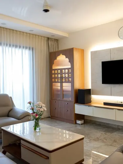This view showcases a complete living area with a comfortable sofa set, a sleek TV unit with ambient backlighting, and a dedicated pooja unit, demonstrating how different functional zones can coexist harmoniously.