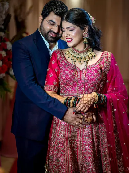 A happy and loving embrace between the couple at their reception. The bride's ornate pink lehenga shines under the lights.