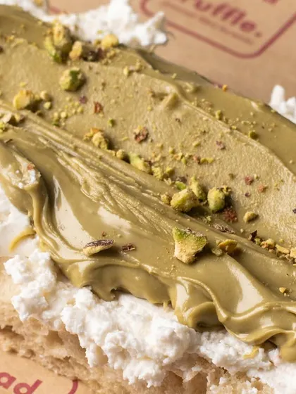 A close-up of a focaccia slice topped with creamy ricotta and pistachio spread. The texture and layers are the main focus of this appetizing shot.