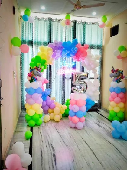 A magical unicorn-themed birthday setup for a 5th birthday. This decoration features a pastel rainbow balloon arch, unicorn figures on cloud-like balloon pillars, and a large silver number "5" balloon.