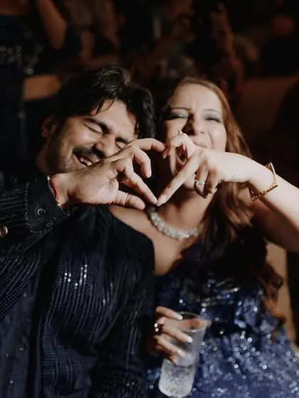 A sweet, candid moment where the couple makes a heart shape with their hands, smiling happily at their cocktail party.