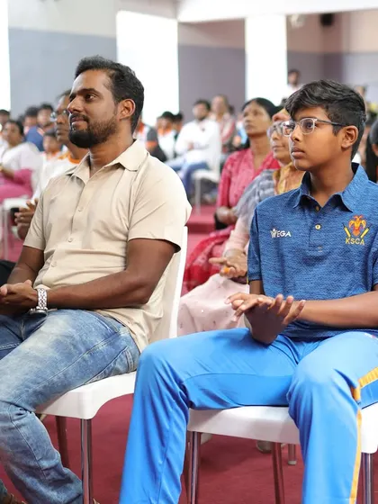 A young cricketer sits in the audience during a felicitation ceremony, inspired by the achievements of his senior.